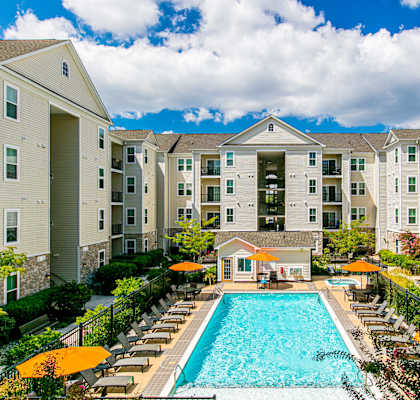 A large swimming pool surrounded by lounge chairs and umbrellas in front of apartment buildings. at Kensington Place Apartments, Woodbridge, VA, 22191