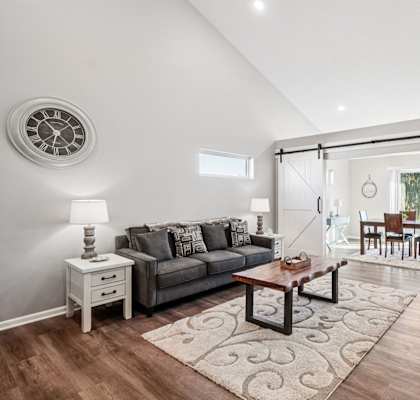A living room with a grey couch, a coffee table, and a clock on the wall.