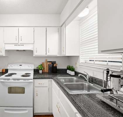 A white kitchen with a black countertop and a white stove.