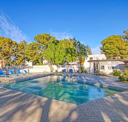 a swimming pool with blue chaise lounge chairs and trees in the background
