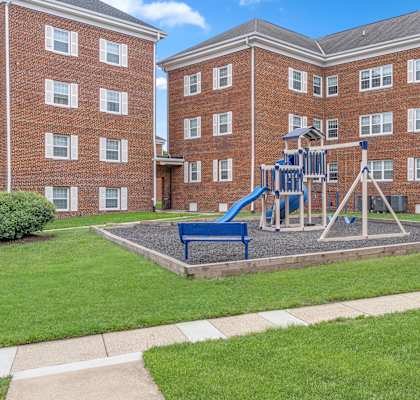 A playground with a blue slide is in front of a red brick building.