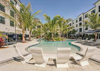 A pool surrounded by palm trees and white chairs at The Stadler Luxury Apartments, Florida 34210
