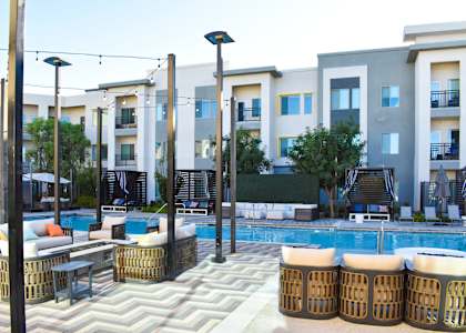 A pool area with a white and grey patterned tile and several wicker chairs and tables.