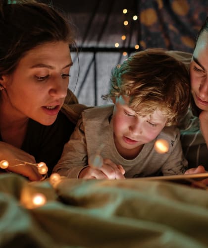 a family lying on a bed reading a book with christmas lights around them