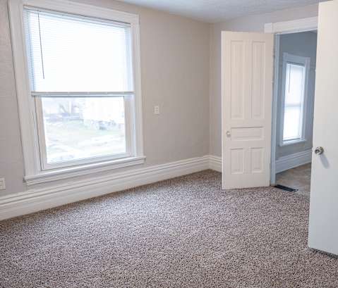 A room with a carpeted floor, a window, and a door.
