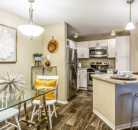a dining area with a glass table and chairs and a kitchen with stainless steel appliances at Fusion Apartments, Orlando, FL 32818
