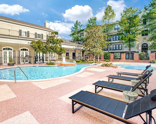A pool surrounded by lounge chairs and trees.