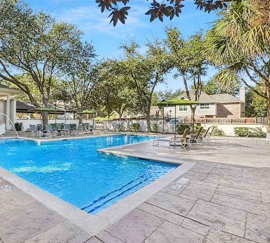 A large swimming pool surrounded by trees and a building in the background.
