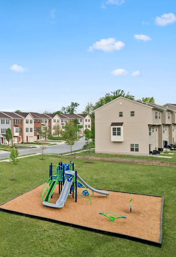 A playground with a green and blue slide in the middle of a grassy area.