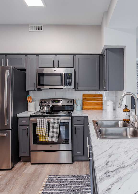 A kitchen with a refrigerator, microwave, oven, and sink.