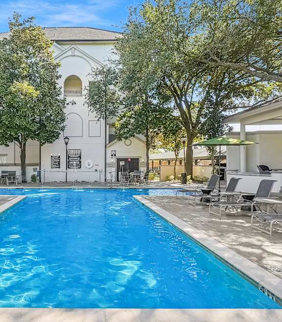 A large swimming pool surrounded by lounge chairs and trees.