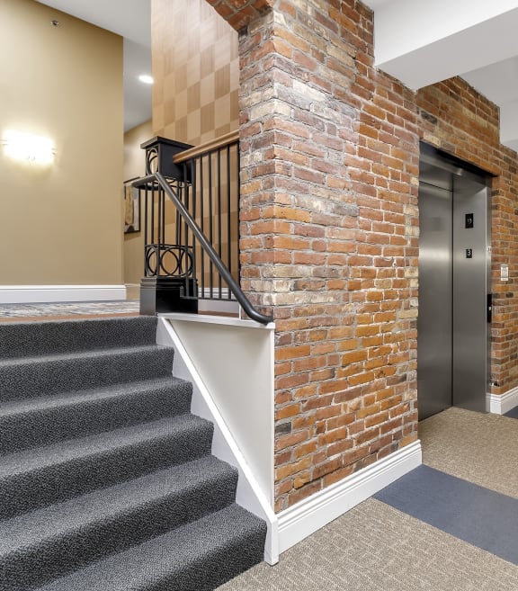 A hallway with a brick wall and a metal staircase at The Granite Works Apartments , Buffalo, NY, 14202