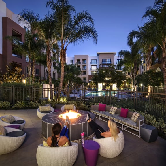 A couple sitting on a couch in a courtyard with a fire pit in the middle. at West Park Apartments, San Diego, California