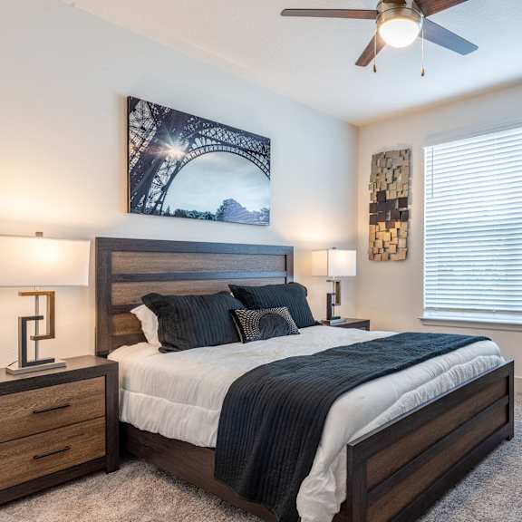 A bedroom with a bed, two lamps, a ceiling fan, and a picture of the Eiffel Tower on the wall.