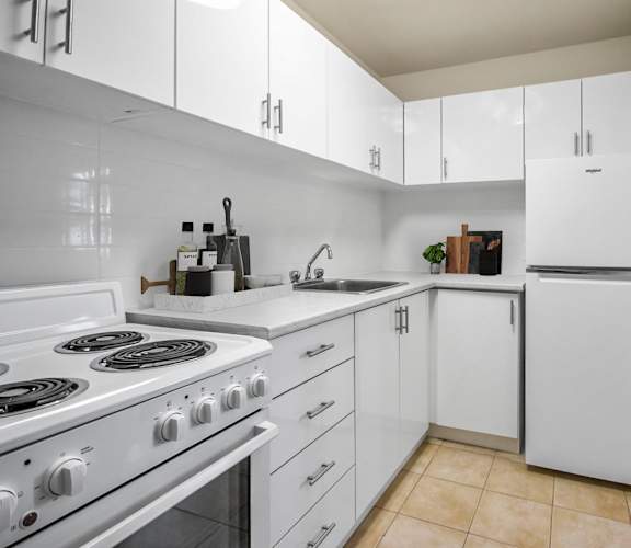A white kitchen with a stove, sink, and refrigerator.