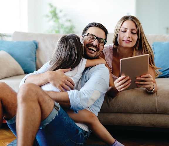 A man is hugging a woman while she looks at a tablet.