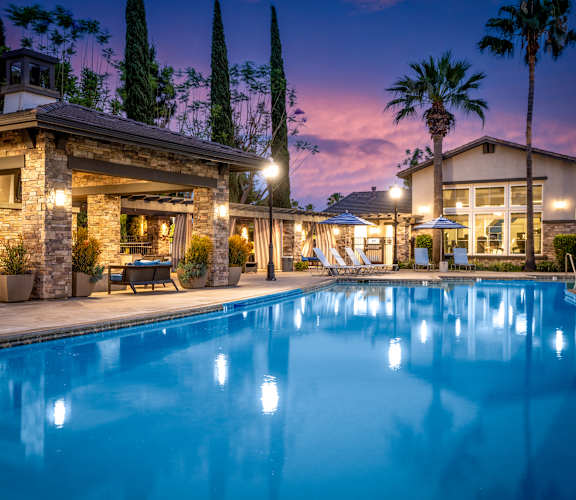 A swimming pool in front of a house with lights on.