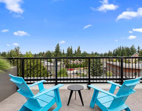 a pair of blue adirondack chairs sit on a patio with a table and stool at Arabella Apartment Homes in Shoreline, WA