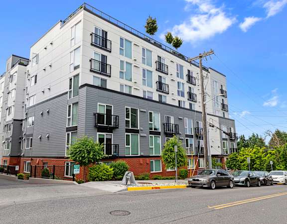 a picture of a grey and brick apartment building with cars parked in front of it at Arabella Apartment Homes in Shoreline, WA