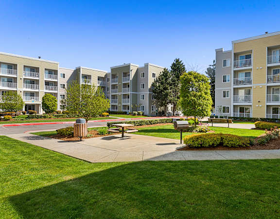 an open area with benches and trees in front of an apartment building at Camelot Apartment Homes in Everett, WA