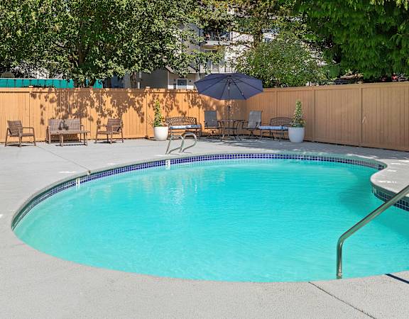 a pool with a fence around it and a patio with chairs and an umbrella  at Casa Blanca Apartment Homes, Everett, WA, 98204