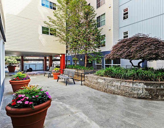 a courtyard with benches and potted plants in front of an apartment building at Promenade at the Park Apartment Homes in Seattle, WA