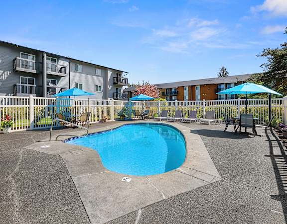a swimming pool with umbrellas in front of an apartment building at Pacific Park Apartment Homes, Edmonds, Washington 98026
