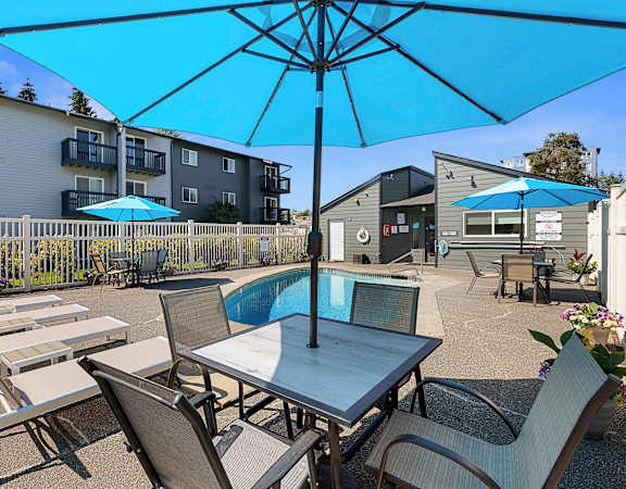 a patio with a pool and chairs and umbrellas at Pacific Park Apartment Homes, WA 98026