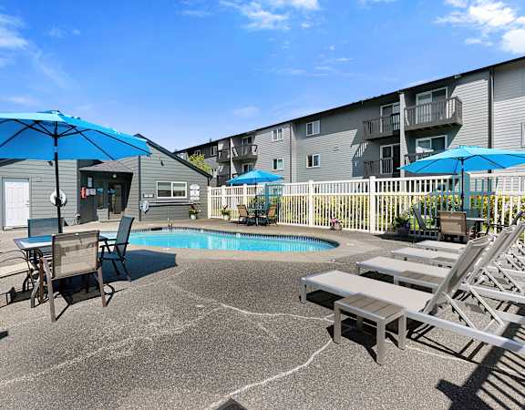 a patio with a pool and tables with umbrellas at Pacific Park Apartment Homes, Edmonds, Washington 98026