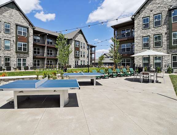 two ping pong tables in a courtyard with apartments in the background at The Depot Luxury Apartment Homes, Raymore, MO, 64083