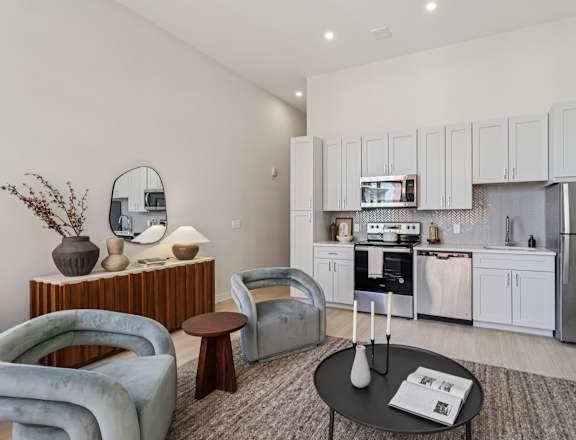 A modern living room with a grey sofa, a coffee table, and a kitchen in the background. at LiveWell Apartments, Pittsburgh, PA, 15222