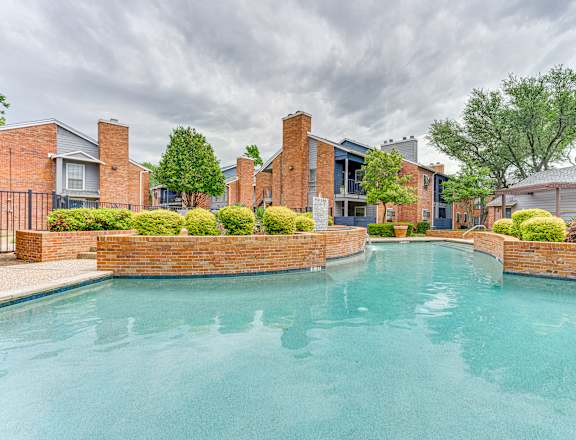 A swimming pool surrounded by a brick wall and residential buildings.