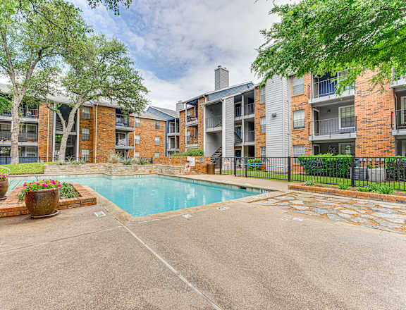A pool surrounded by a brick building and trees.