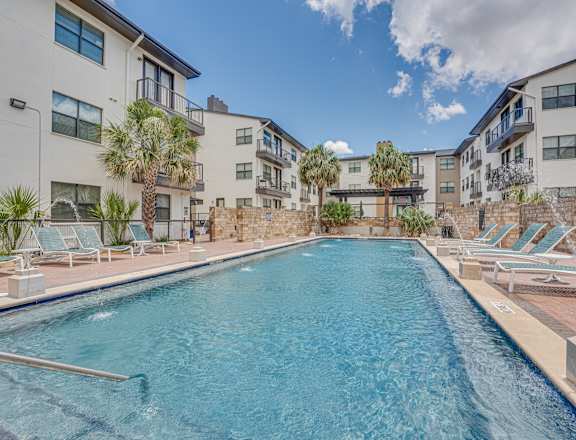 A swimming pool surrounded by lounge chairs and buildings.