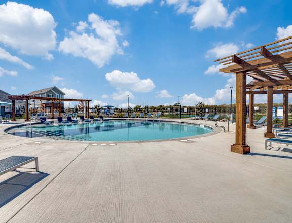 A large outdoor swimming pool surrounded by a wooden pergola and benches.