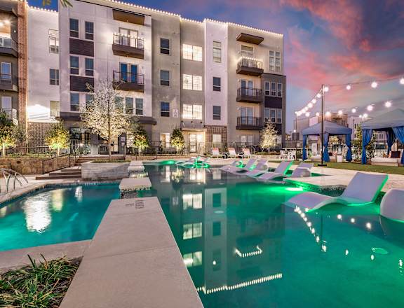 A swimming pool in front of a building with lights around it.