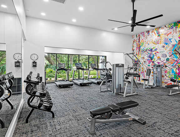 A gym with a variety of equipment and a colorful mural on the wall.
