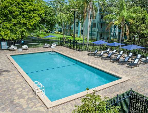 a swimming pool with lounge chairs and umbrellas in front of an apartment building  at Club at Emerald Waters, Hollywood, FL