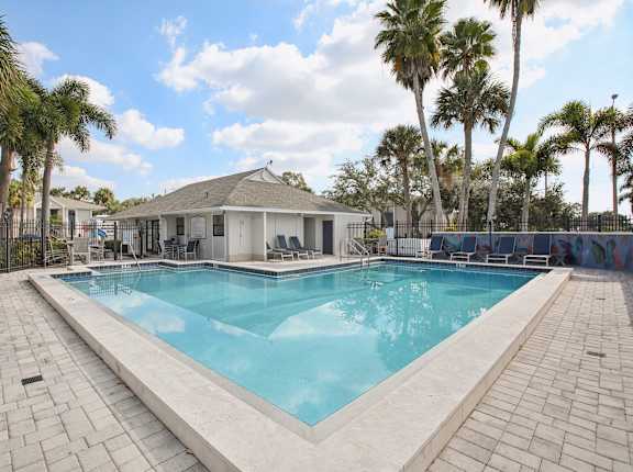 A pool surrounded by palm trees and a white building.
