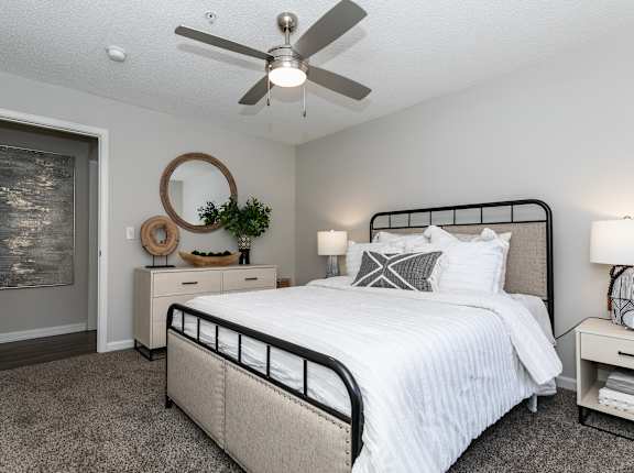 A bedroom with a large bed, a ceiling fan, and a painting on the wall.