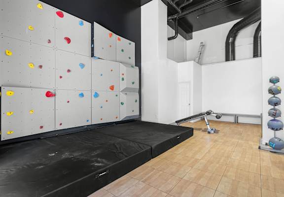 A climbing wall with various colored holds and a mat on the floor.