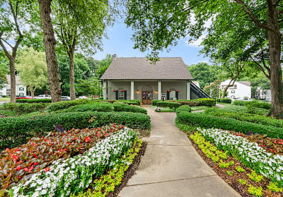 A small building is surrounded by a garden with a concrete walkway leading to it.