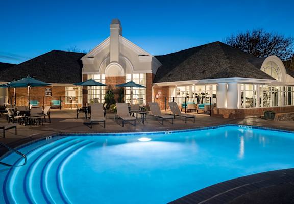 A swimming pool in front of a house with a lit up poolside area.