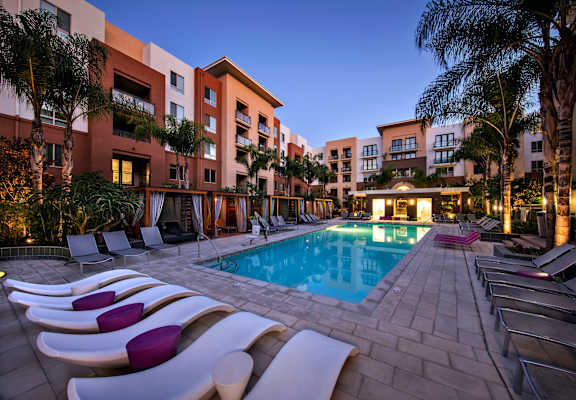 A pool surrounded by lounge chairs and palm trees. at West Park Apartments, San Diego