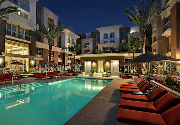 A swimming pool surrounded by red lounge chairs and umbrellas at night. at West Park Apartments, California
