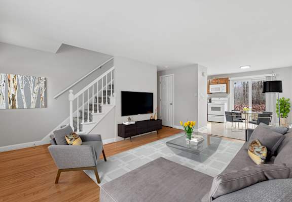 A living room with a grey couch, a grey armchair, a glass coffee table and a television.