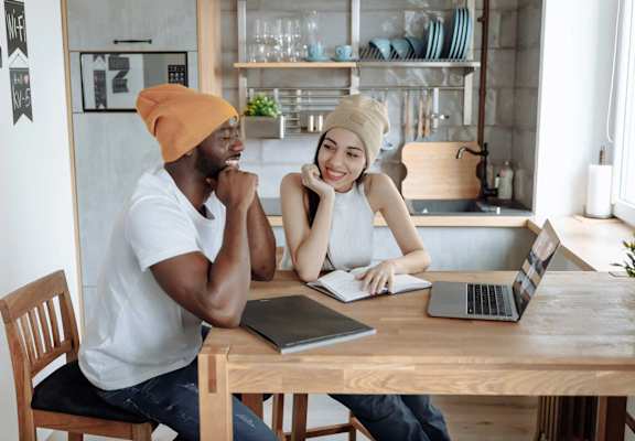 Two people sitting at a table with laptops and notebooks.