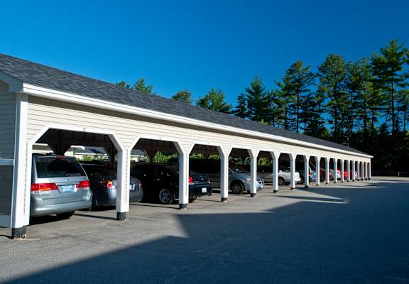 A long row of cars are parked under a covered parking structure.
