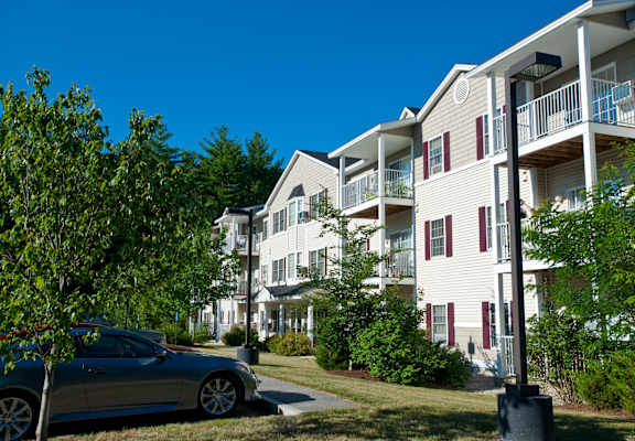A silver car is parked on a street in front of a white building with red shutters.