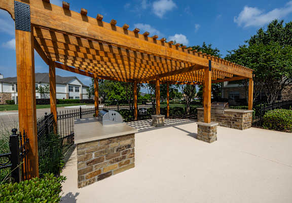 a covered patio with a stone fireplace and a wooden pergola
